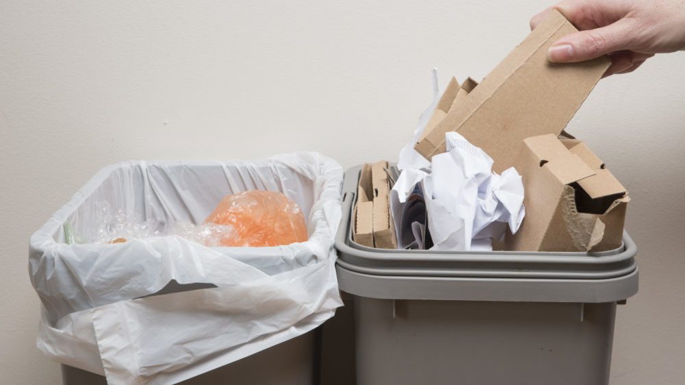 Hand puts cardboard into home trash bin
