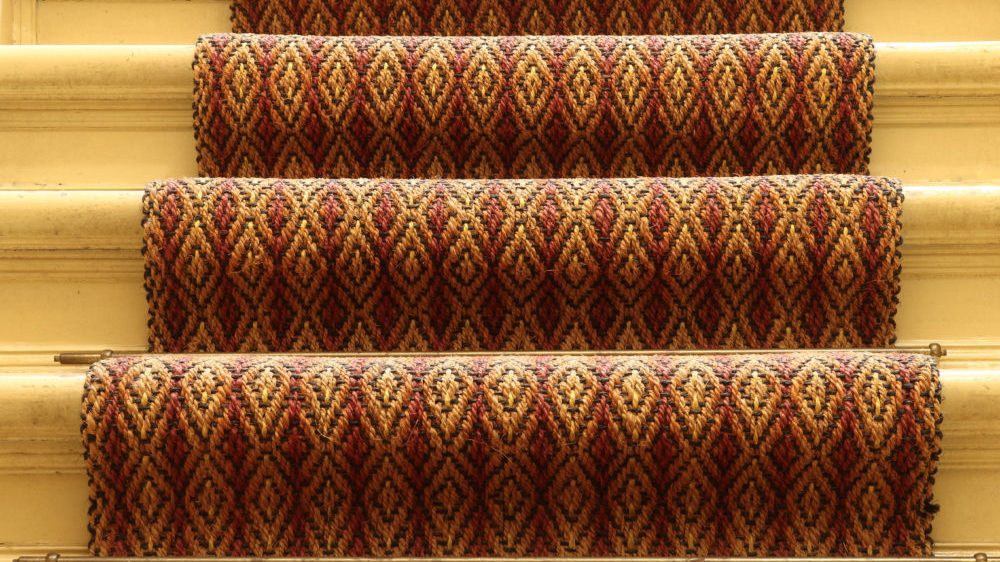 Textured carpet runners in red and gold pattern on light hardwood stairs.
