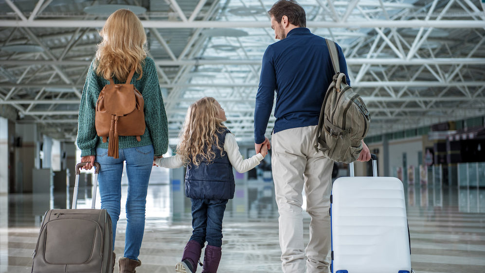 Glad parents and child passing terminal after plane landing. They are waiting for their shipped belongings for their new home.