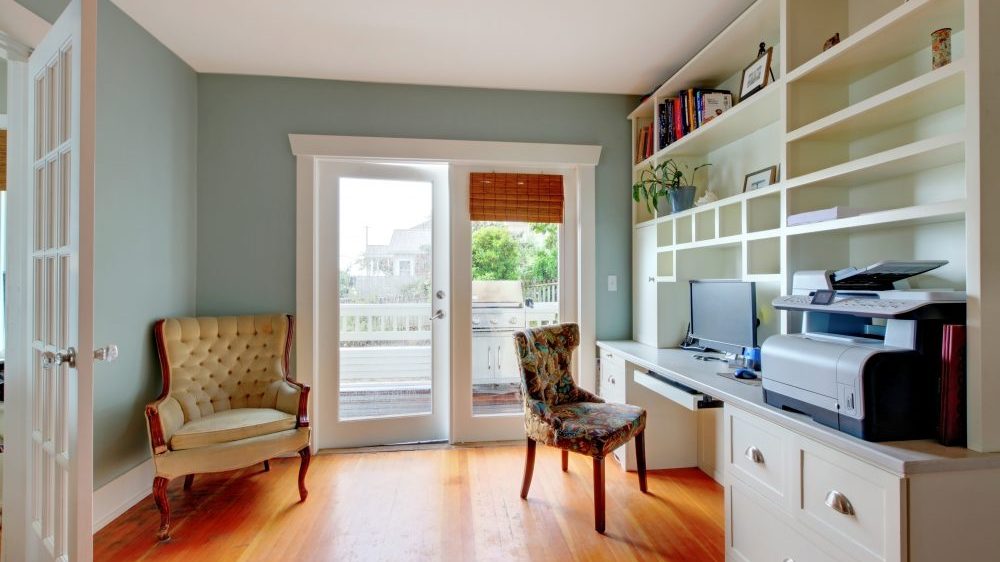 Living room converted to a home office with green walls and white shelves.