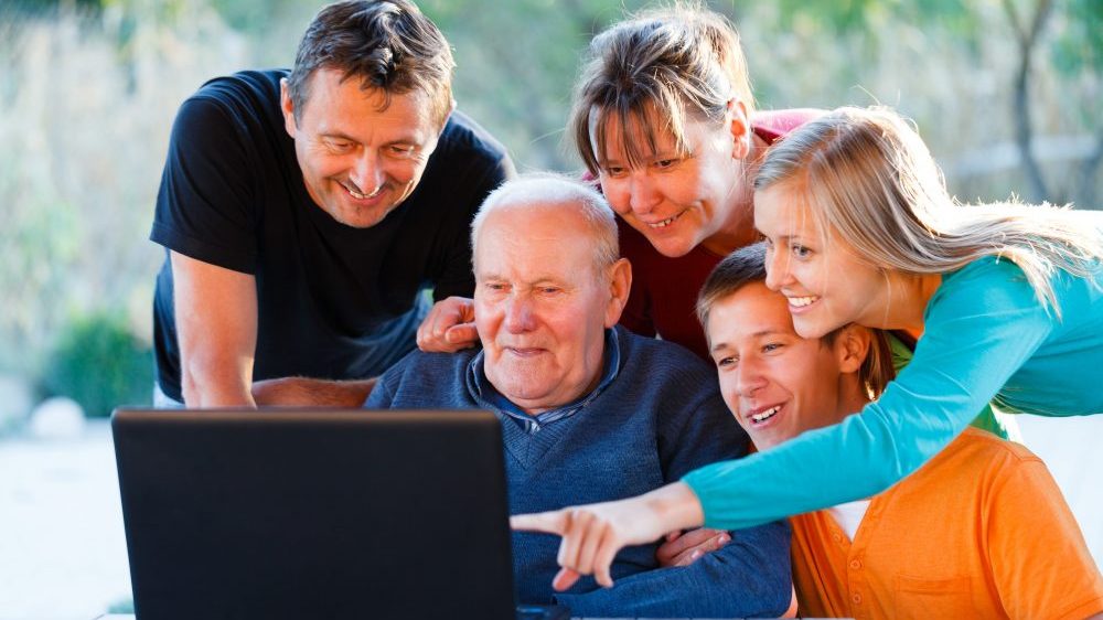 Three generations of a family are looking at homes for sale on laptop.