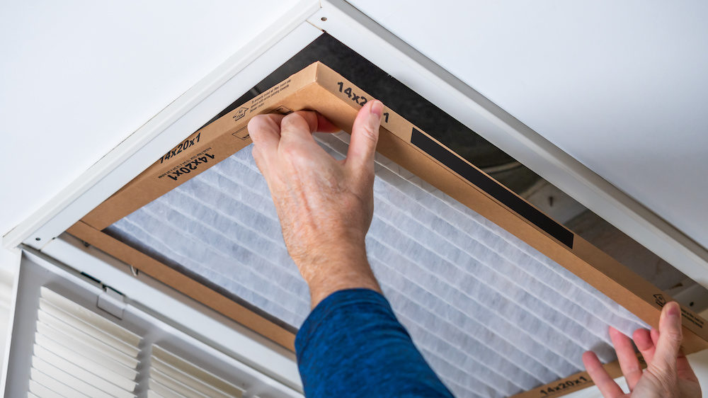 A man replacing a dirty HVAC air filter in a ceiling vent. Home air duct cleaning for clean air.