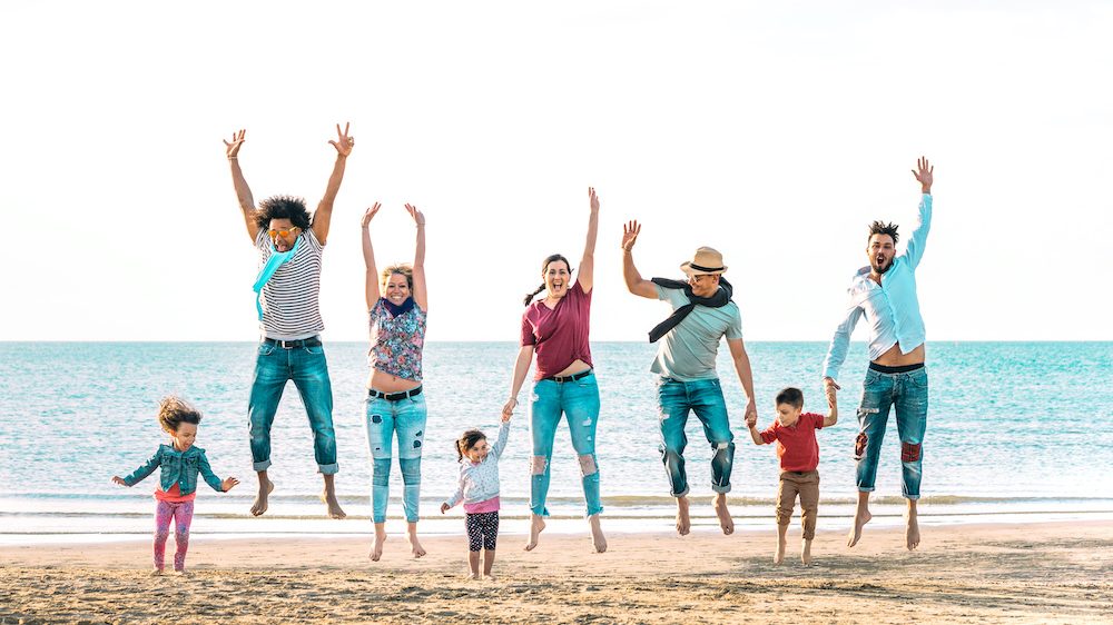 Happy multiracial families jumping together at beach holding hands at their summer vacation home on the beach.