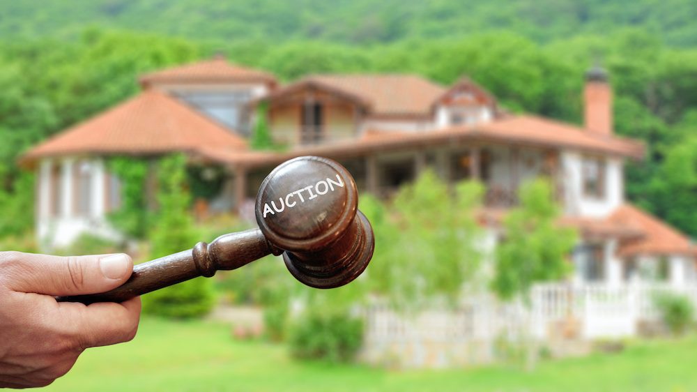 Concept real estate auction,blurred house background and wooden gavel in a hand.