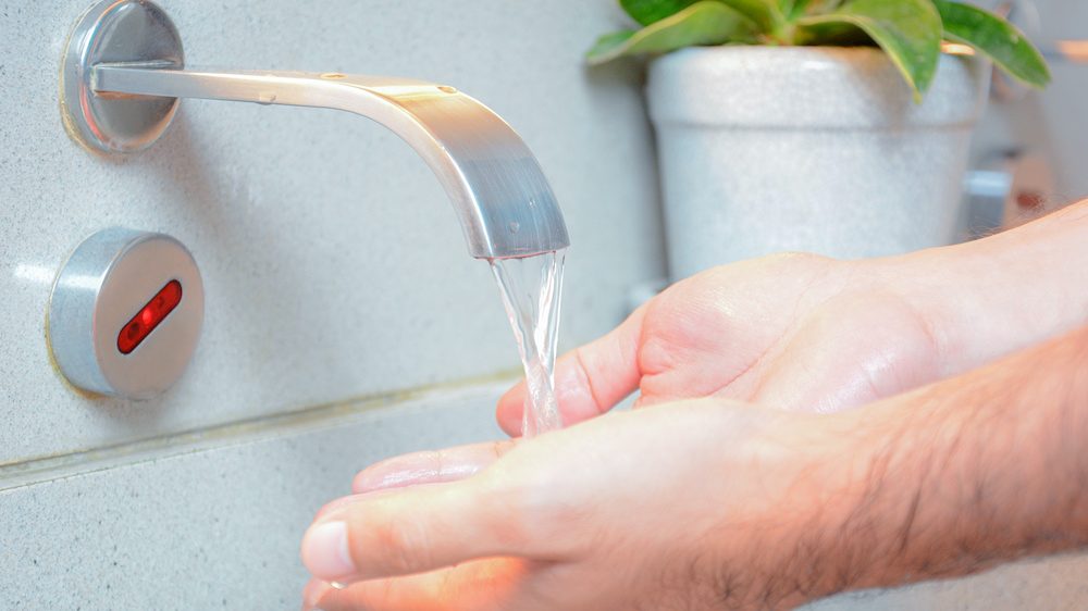 Using a touchless faucet to wash hands in sink.