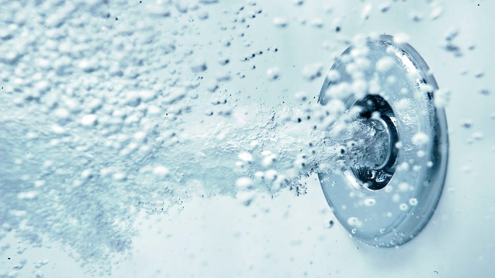 A whirlpool tub jet blows air horizontally under water in a tub full with water.