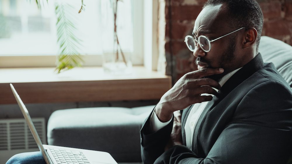Black businessman working from home, isolated by coronavirus. Using laptop to review retirement savings relief during the Covid-19 pandemic.