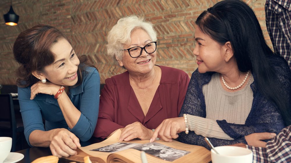 Vietnamese elderly women discussing photos of their youth while decluttering a home to prepare for sale.
