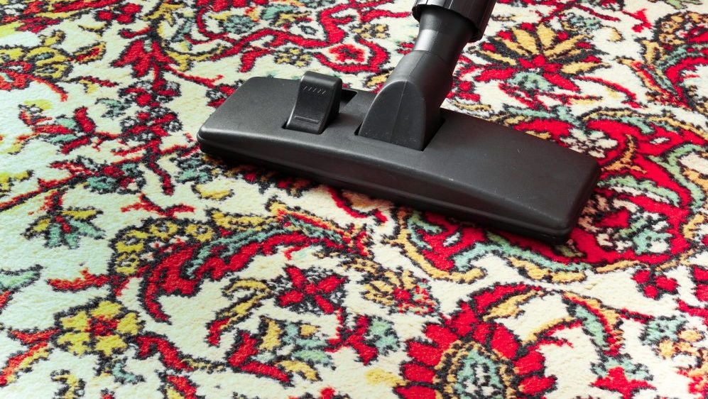 Photo showing how to properly vacuum clean area rugs. Vacuum cleaner universal nozzle moving across oriental rug.