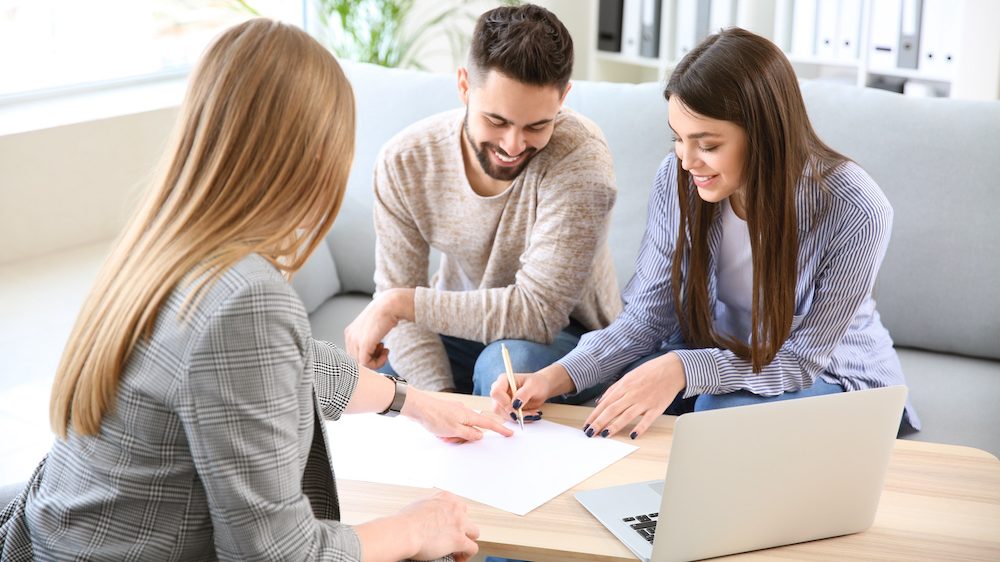 Young couple in office of real estate agent signing a listing agreement to sell their home.