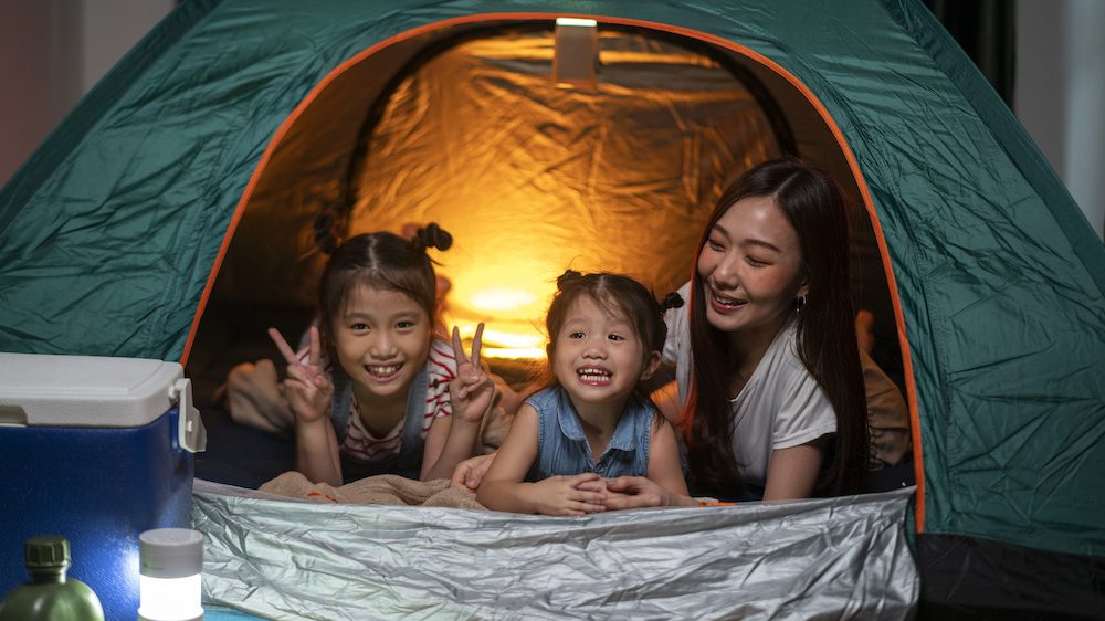 Woman playing and staying in tent with her daughter and having fun with camping tent in their bedroom a staycation lifestyle a new normal for social distancing in coronavirus outbreak situation.