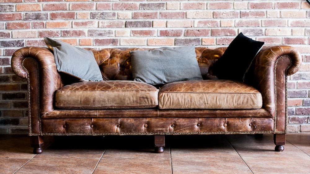 Vintage style of interior decoration with a leather sofa that needs cleaning in against a brick wall in a room.
