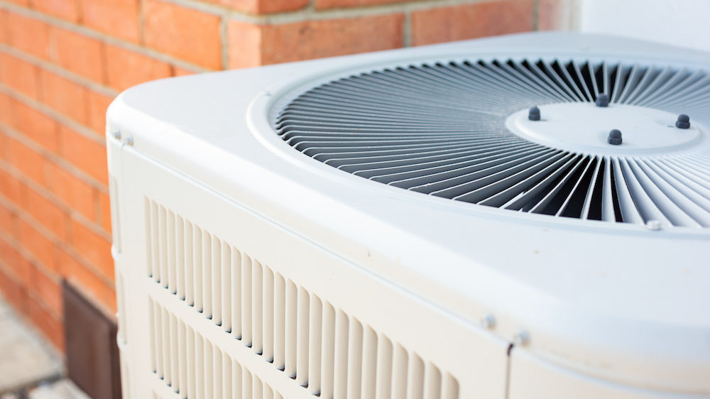 A view of an air conditioner condenser unit in the backyard of a home.