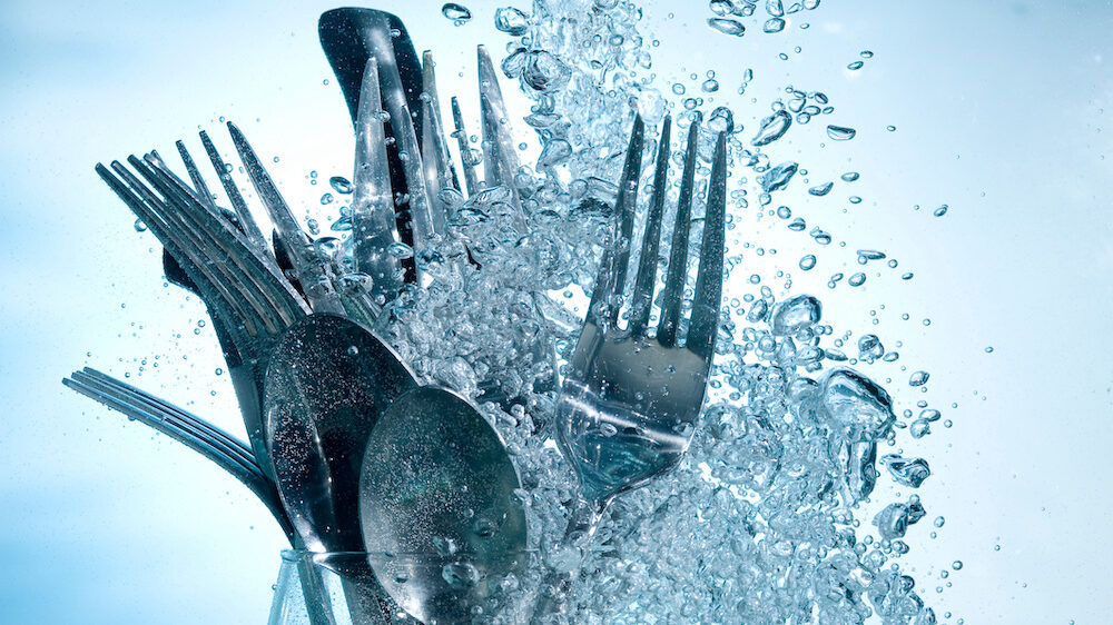 Washing kitchenware in dishwasher with clear water on bubbles background.
